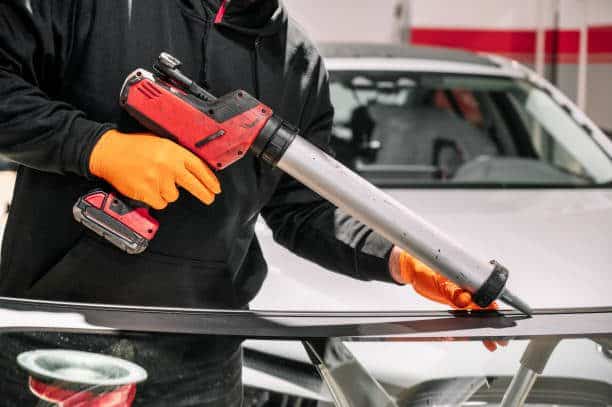 Glazier applying rubber sealing to windshield in garage, close up. High quality photo